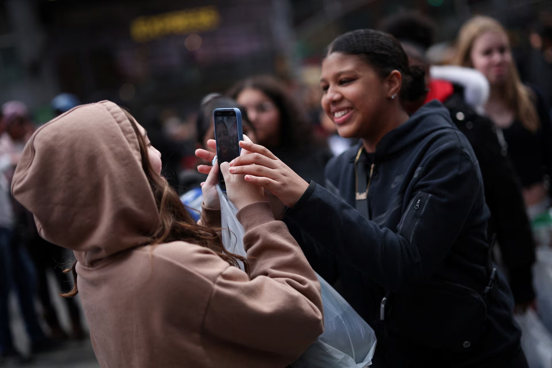 A young woman makes a video of her friends with a mobile phone to post on TikTok in Times Square in  ...